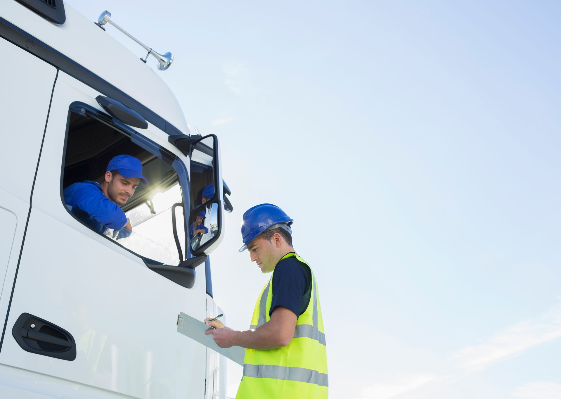 Worker with clipboard talking to truck driver